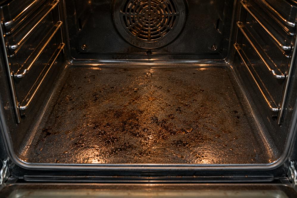 Dirty oven bottom with burnt grease and baked-on food residue