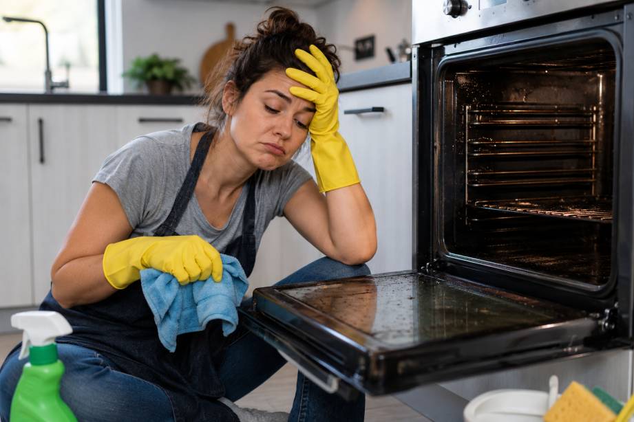 Woman struggling to clean a dirty oven during DIY oven cleaning at home