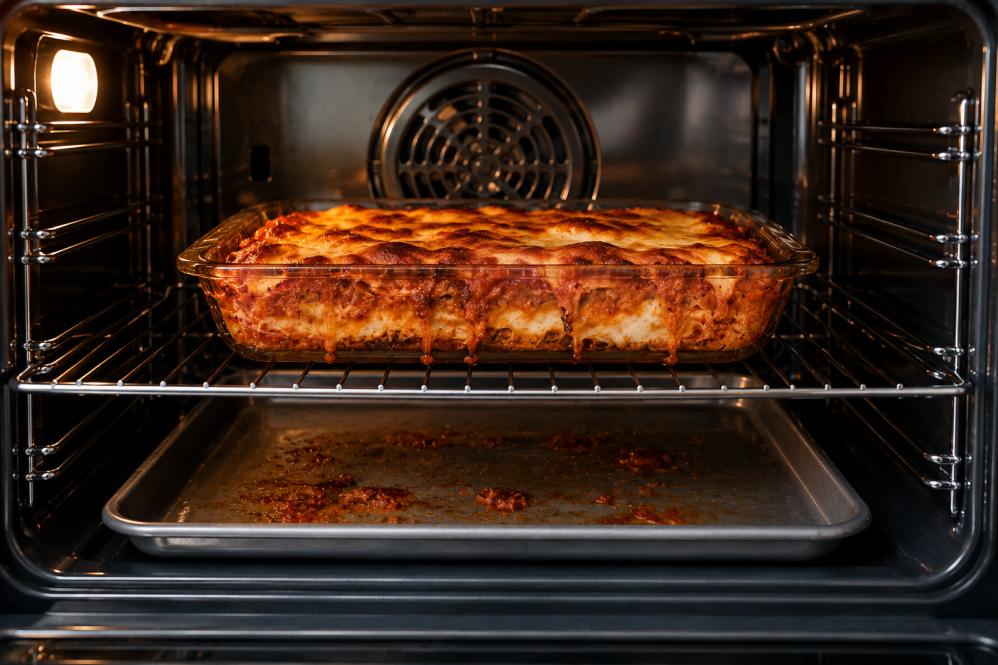 Lasagna bubbling in oven with tray underneath catching food spills and grease